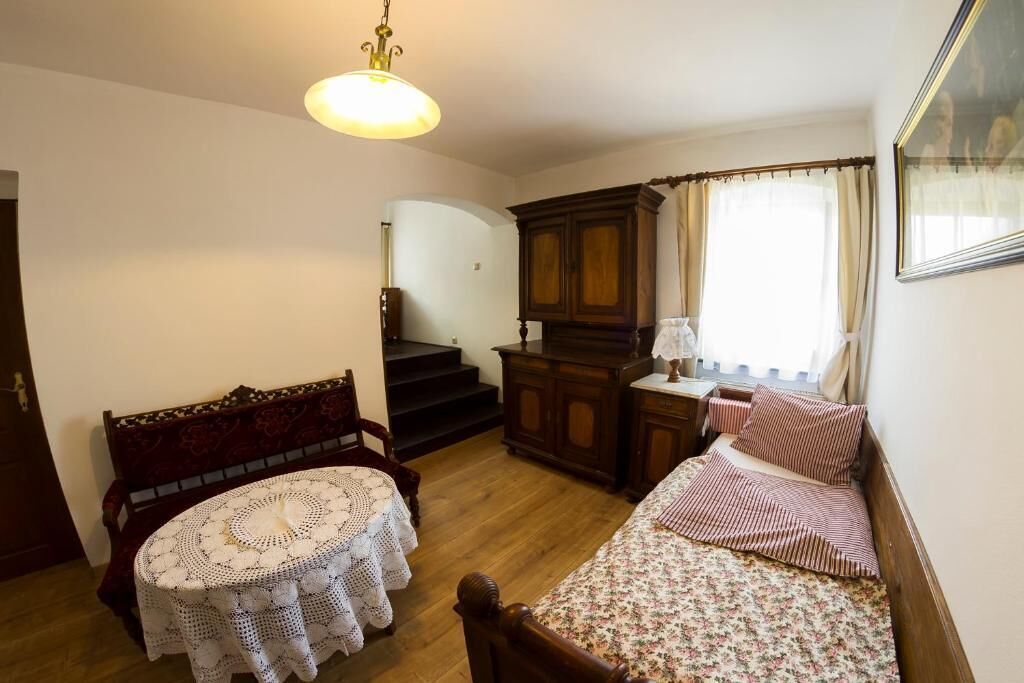 A cozy room with a wooden bed, a round table with a crocheted tablecloth, a wooden cabinet, and a staircase leading to another room.