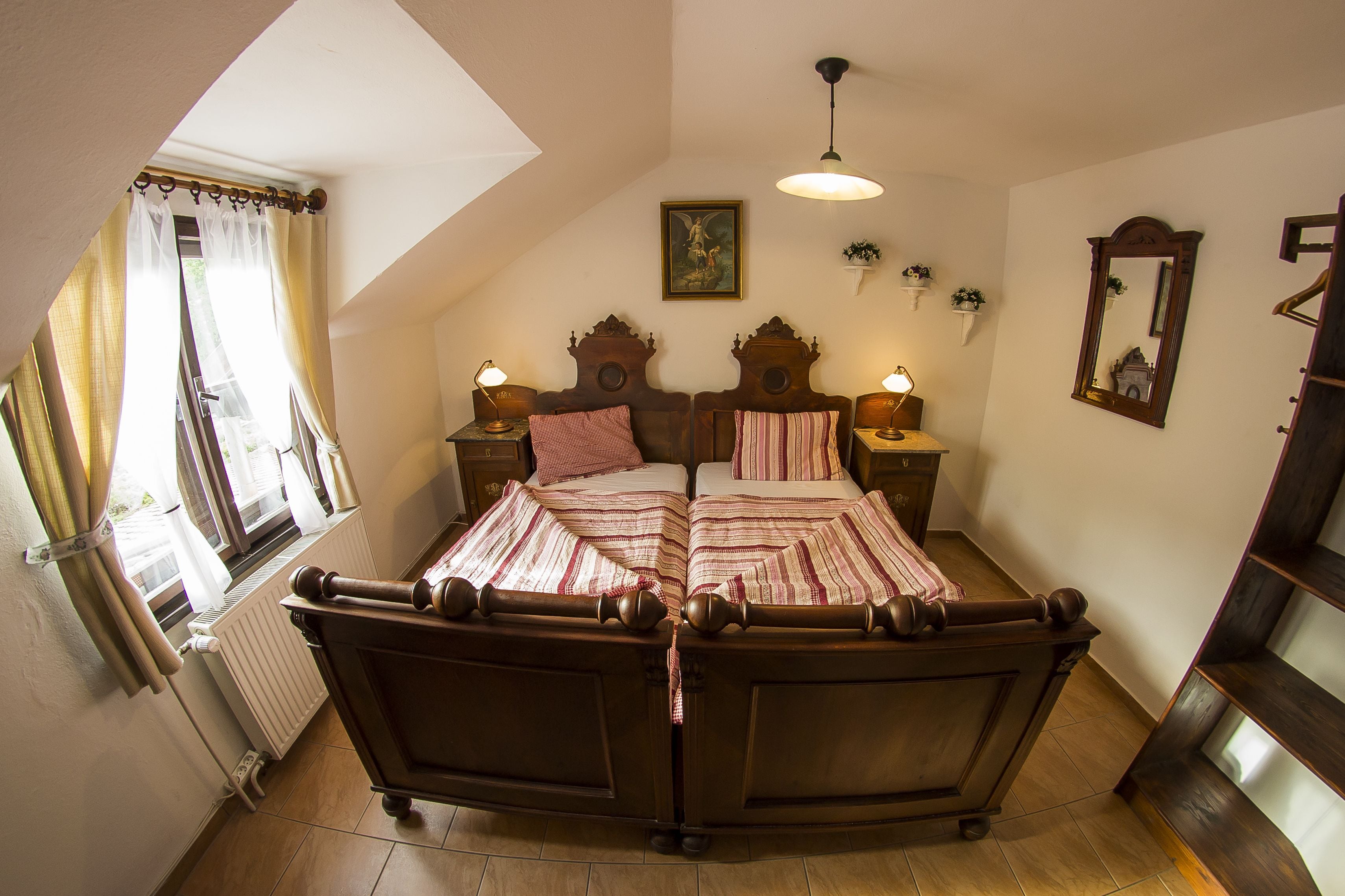 Un dormitorio con una cama grande, dos mesitas de noche, una lámpara colgante, un radiador y una ventana con cortinas.