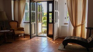 Una puerta abierta que da a un jardín, una silla, una mesa y un tapete en una habitación con suelo de baldosas.