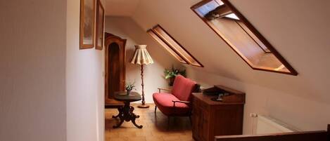 Une chambre mansardée chaleureuse, avec un plafond en pente, un lit en bois, une chaise rouge, une petite table et une lampe.