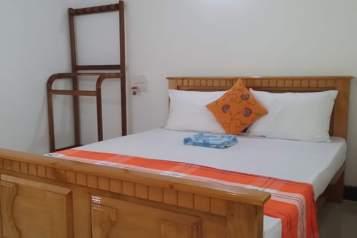 Una cama con cabecera de madera, ropa de cama blanca y un cojín decorativo naranja.