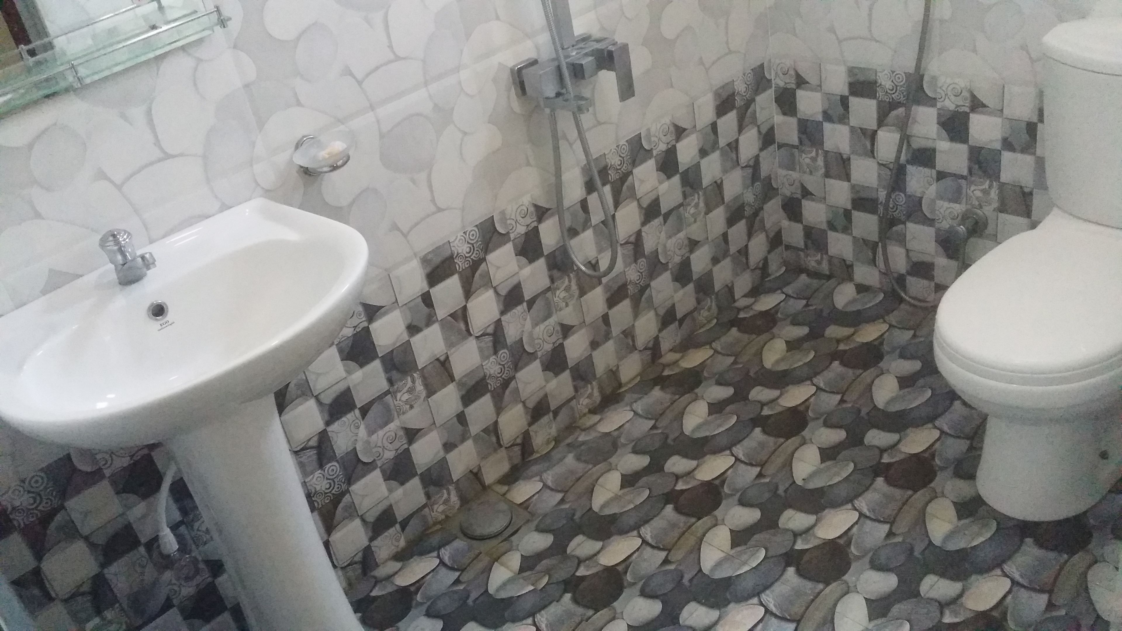 A bathroom with a white sink, a toilet, and a shower area with patterned tiles.