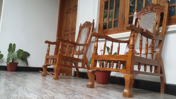 Deux chaises en bois aux motifs complexes, placées sur un sol carrelé, près d’une porte et d’une fenêtre en bois.