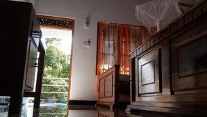 Une chambre avec un lit en bois, une fenêtre ornée de rideaux à motifs floraux orange et une vue sur la verdure à l’extérieur.