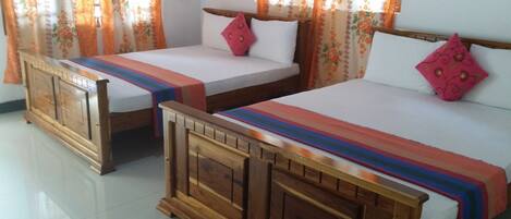 Dos camas de madera con sábanas blancas y colchas a rayas de colores en una habitación con cortinas florales.