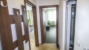 A hallway with wooden doors, a tiled floor, and a view into a room with a plant and curtains. - Flora Apartment Centrum (Sofia)