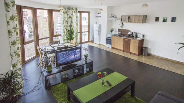 A modern living room with a flat-screen TV, a coffee table, and a dining area with a table and chairs. - Flora Apartment Centrum (Sofia)