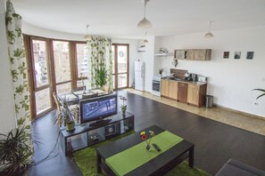 Uma sala de estar moderna com uma televisão de tela plana, uma mesa de centro e um espaço de jantar com mesa e cadeiras.