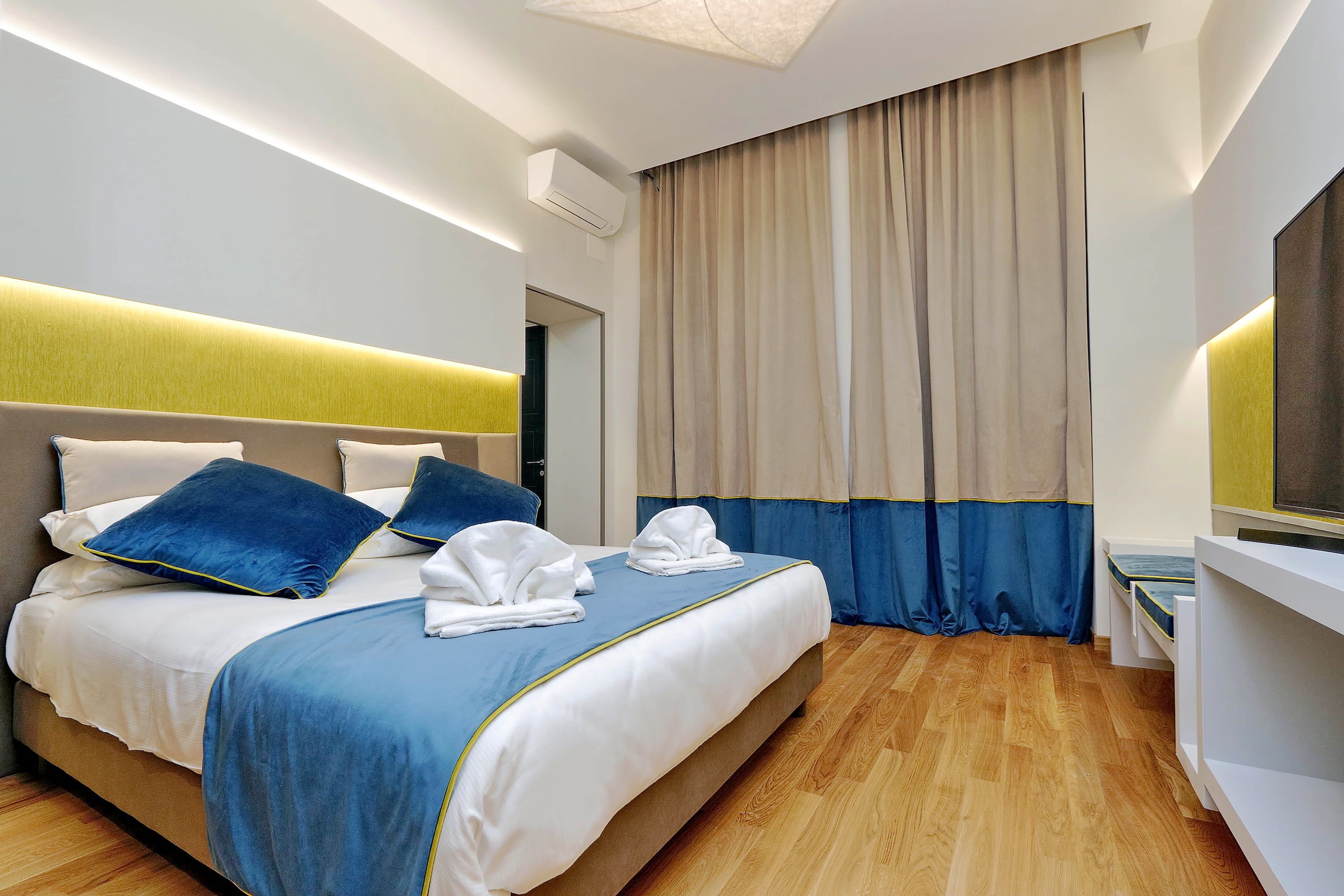 A modern hotel room with a large bed, a bedside table, and a flat-screen TV.