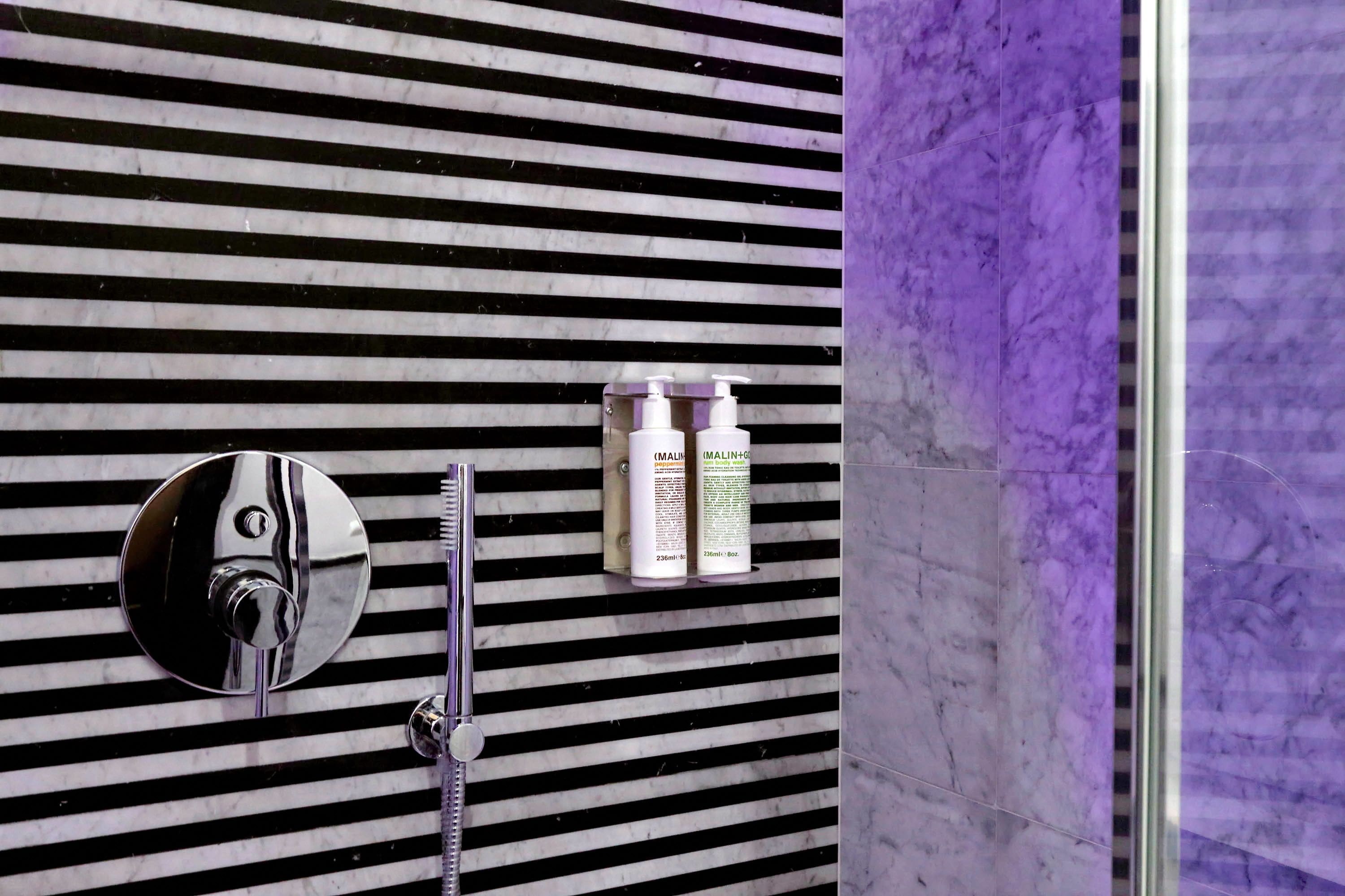 A bathroom with striped black and white tiles, a round mirror, a faucet, and two bottles of lotion on a shelf.