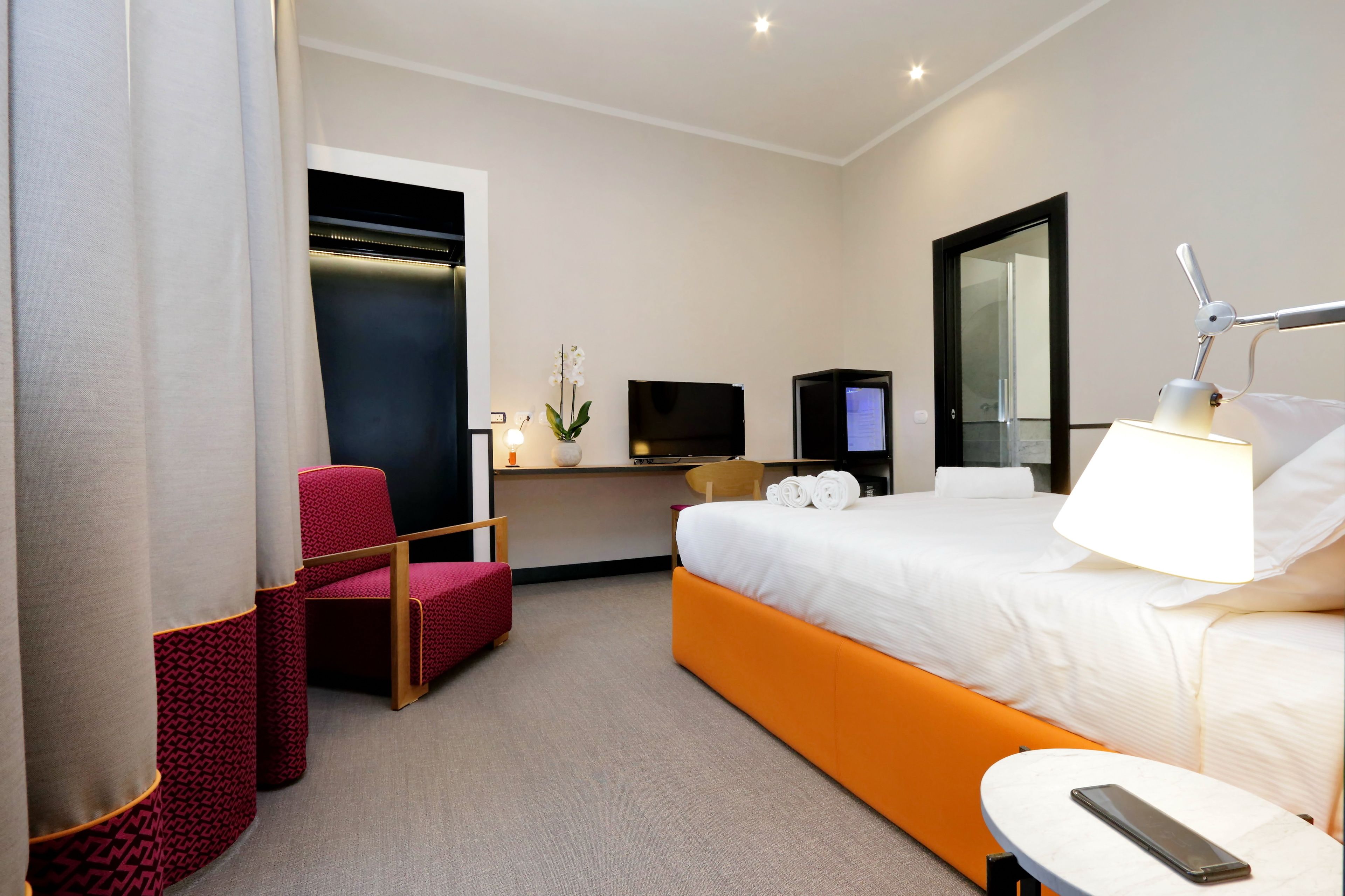 Una habitación de hotel con una cama, un escritorio con televisor, una silla y una lámpara.