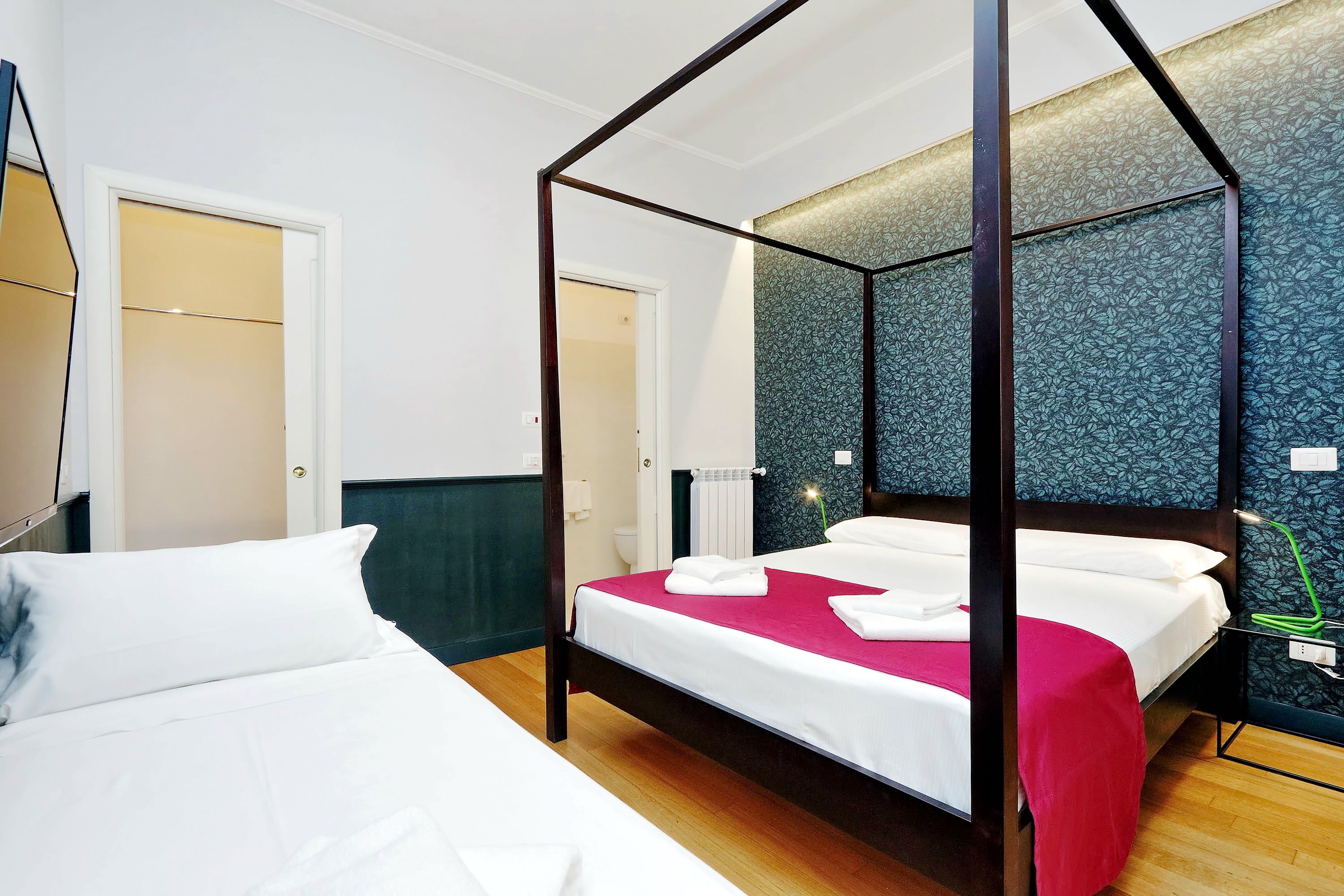 Un lit à baldaquin avec du linge de lit blanc et un détail rouge, un plancher en bois et un mur à motifs.