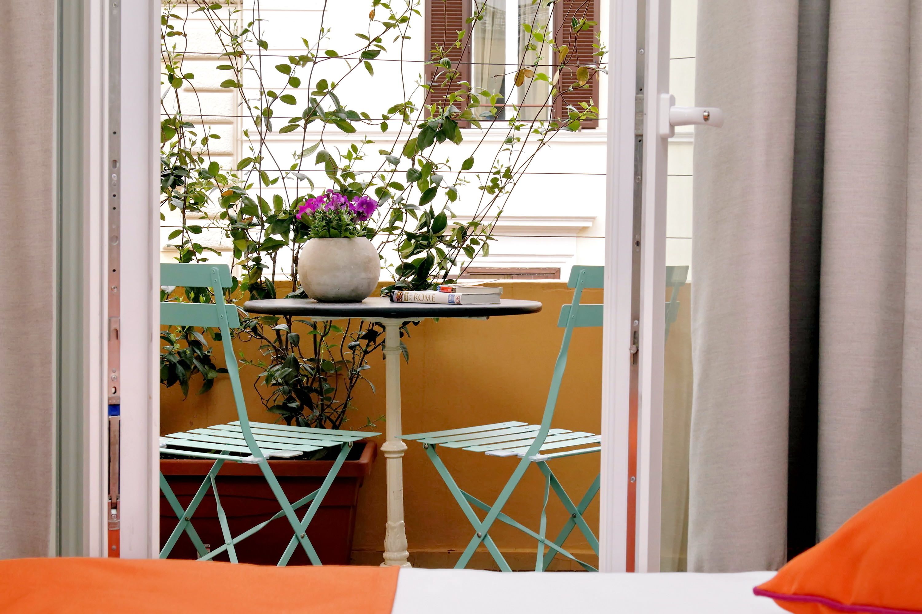 A room with a small table, two chairs, a potted plant, and a window with curtains.