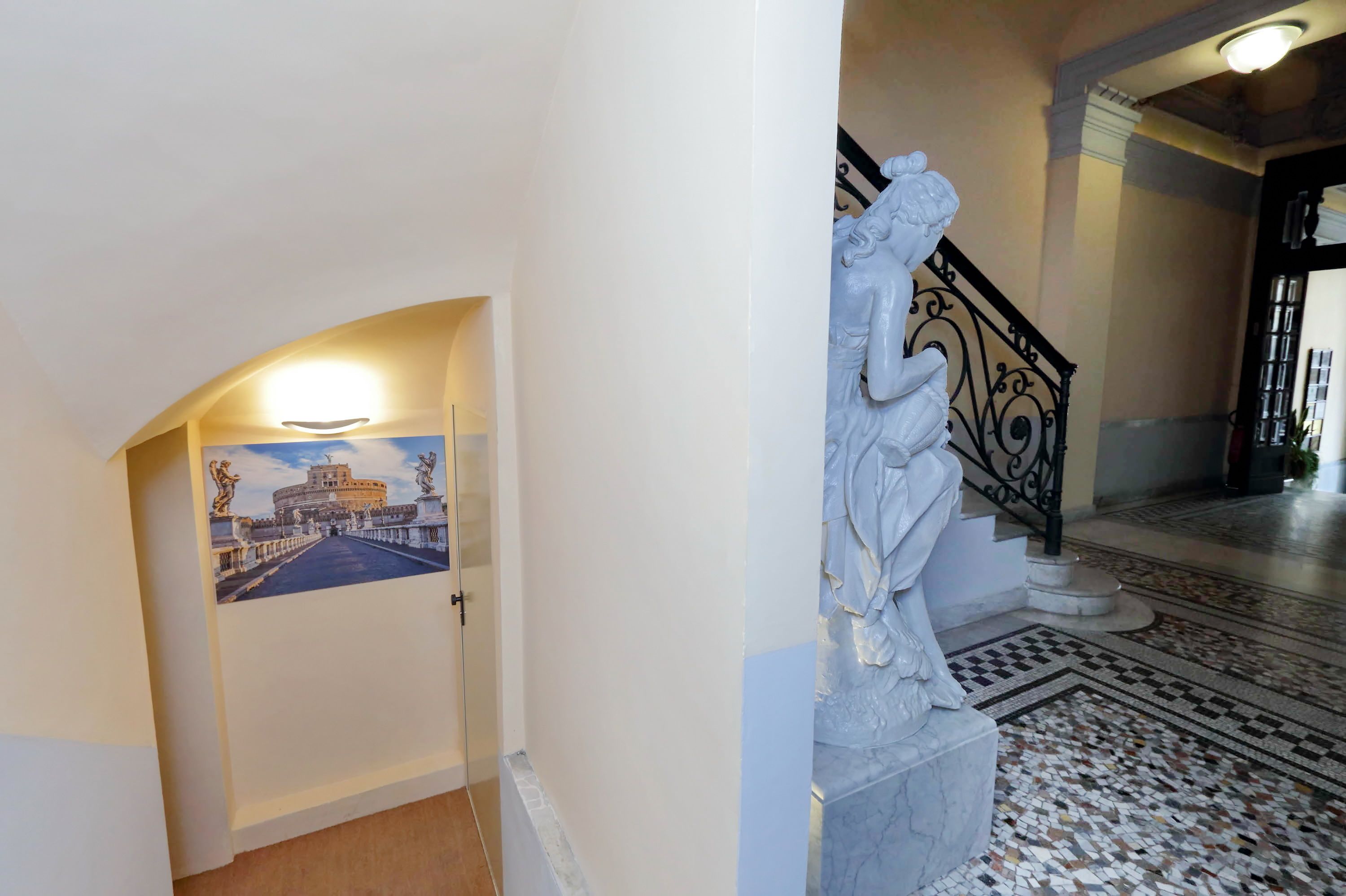 A hallway with a marble staircase, a mural of a historical building, and a patterned floor.