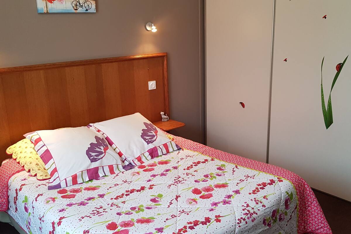 A bedroom with a wooden headboard, a floral bedspread, and a wardrobe with a mirror.