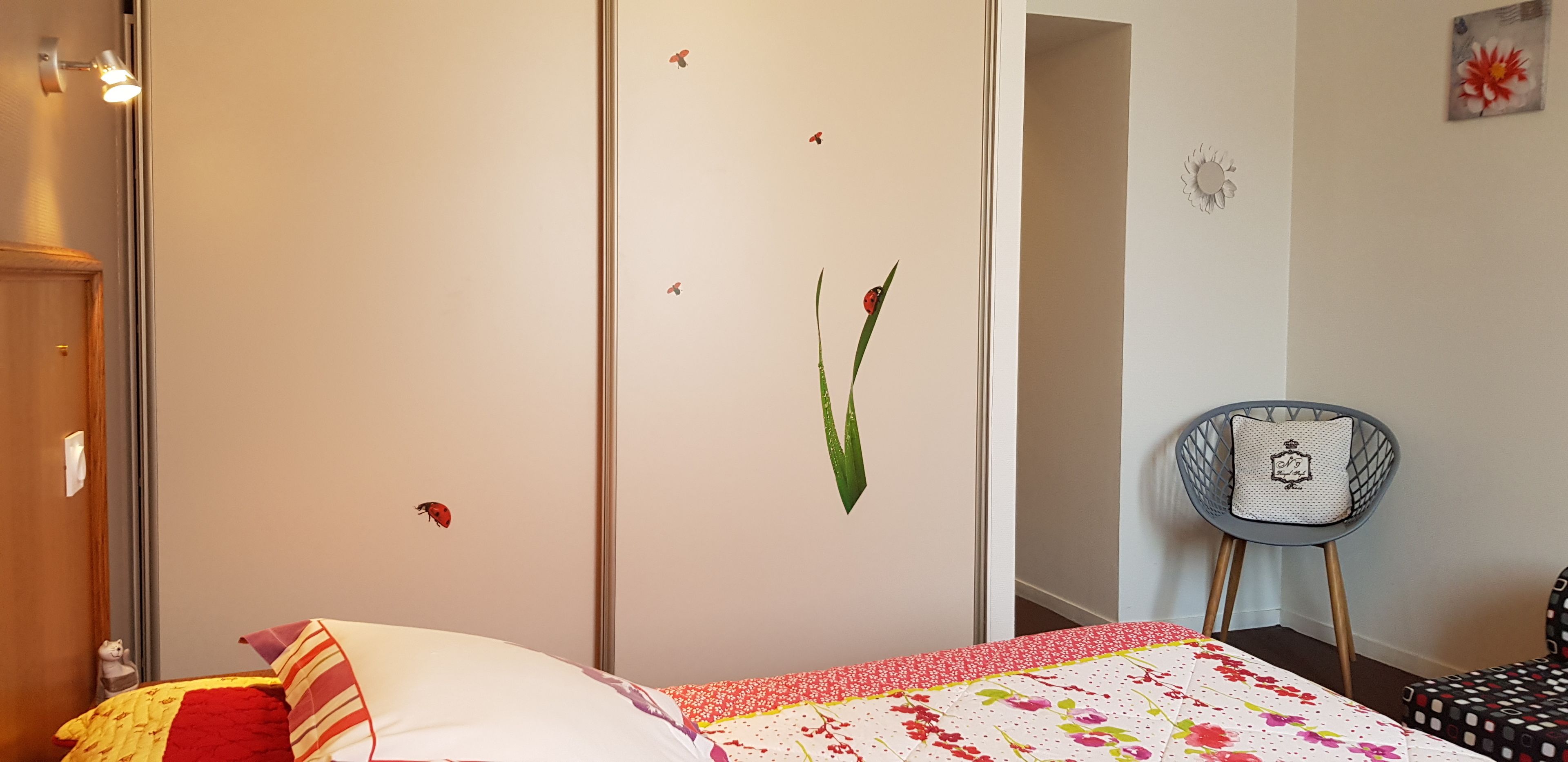 A bedroom with a bed, a chair, and a wall with decorative elements.