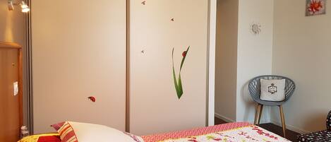 A bedroom with a bed, a chair, and a wall with decorative elements.