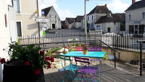 A patio area with a table and chairs, a flower pot, and a signpost with directions. - Au Bosquet Fleuri (Martizay)