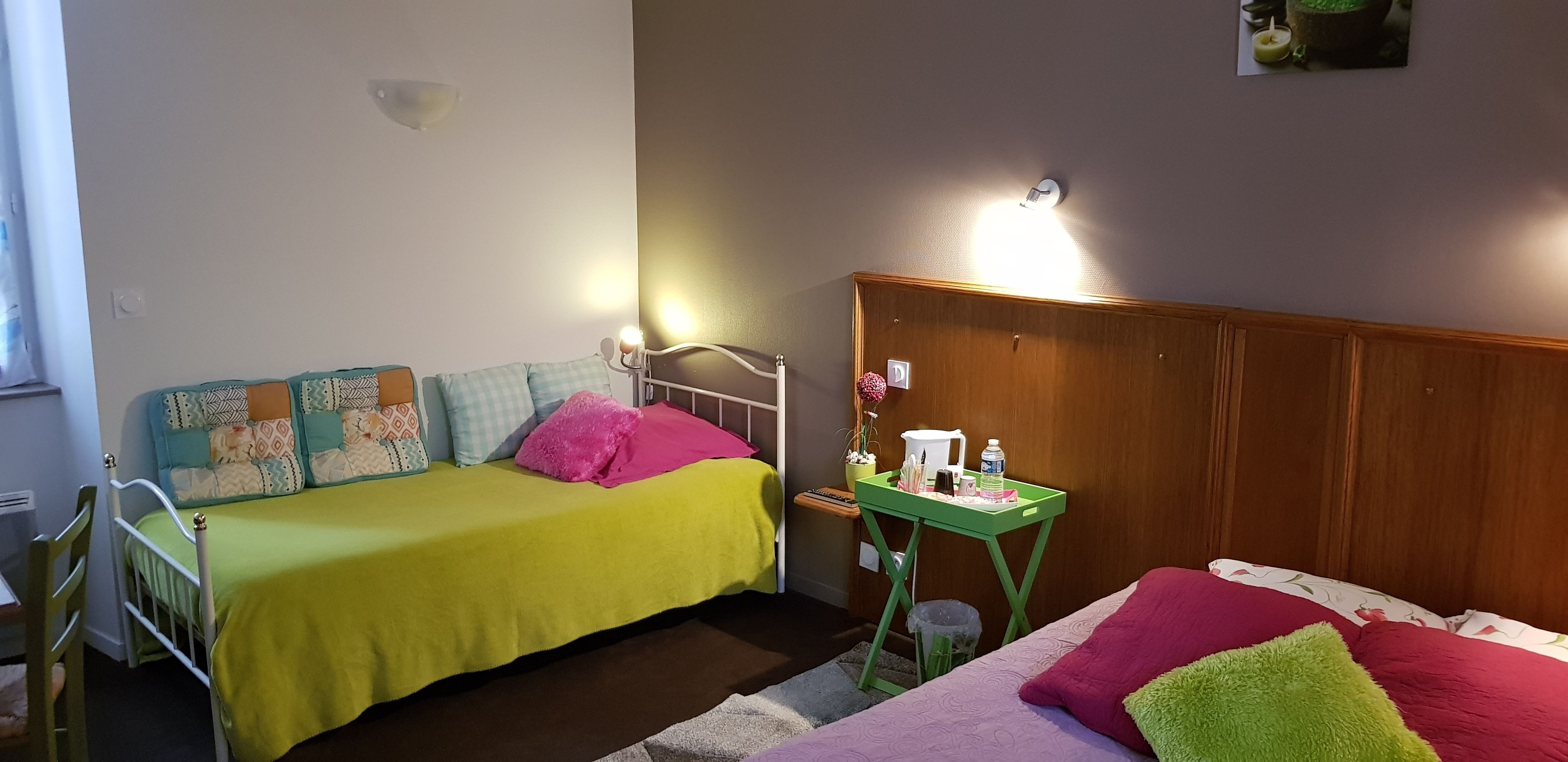 Une petite pièce agréable, dotée de deux lits, d’une tête de lit en bois, d’une table de chevet avec une lampe et d’une petite poubelle.