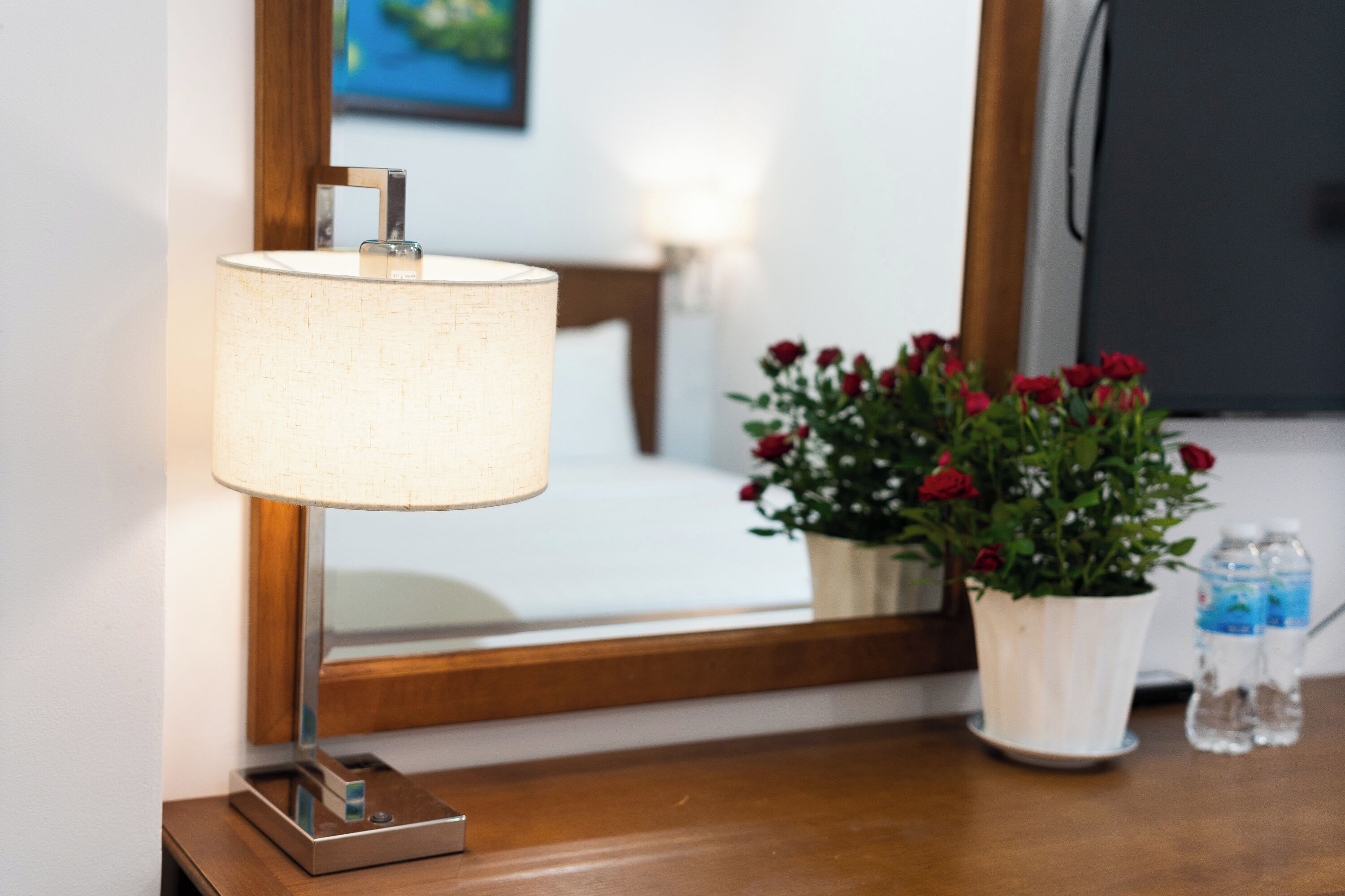 Een nachtkastje met een lamp, een bloeiende plant in pot en twee waterflessen.