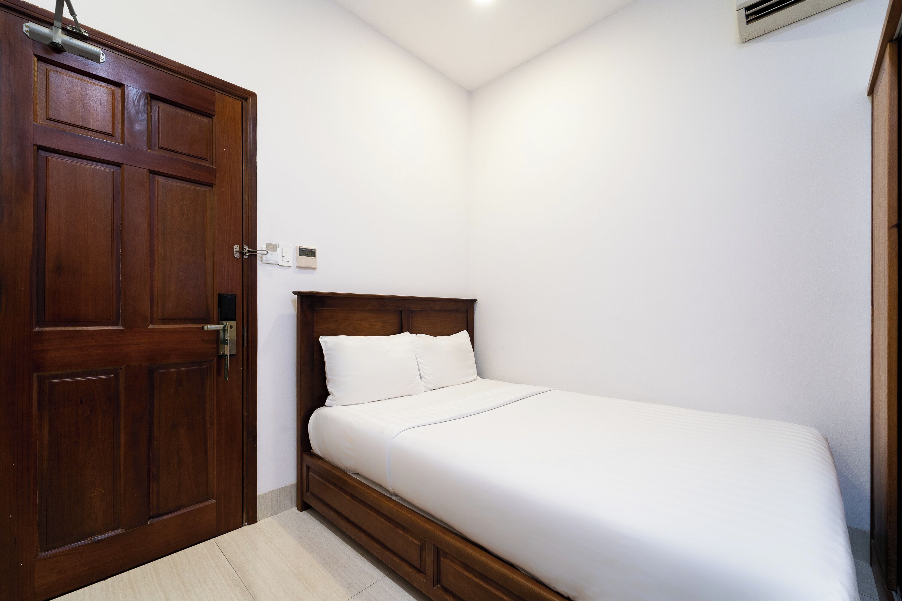 A bedroom with a wooden door, a bed with white bedding, and a small bedside table.