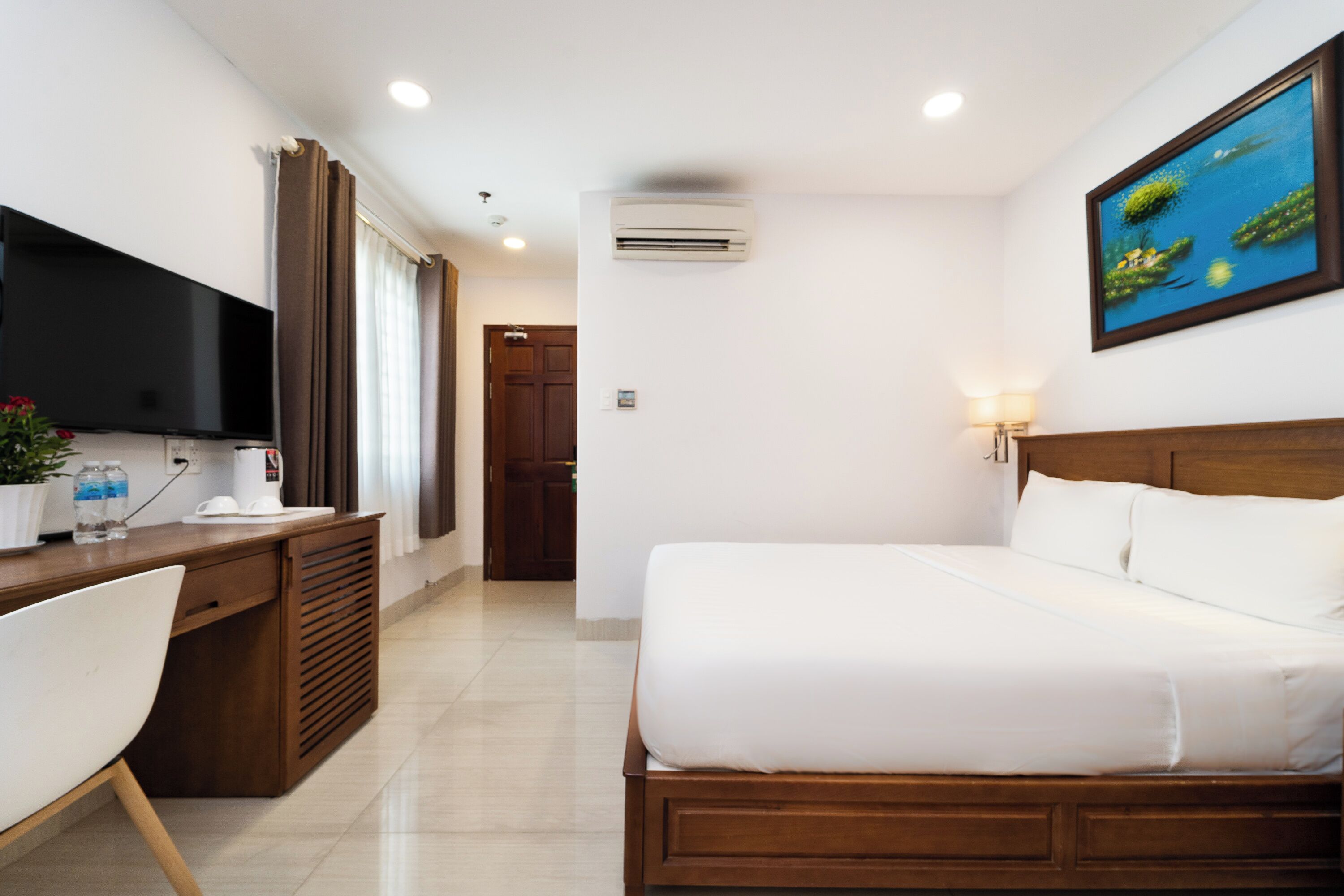 A hotel room with a bed, a desk with a flat-screen TV, a chair, and a painting on the wall.