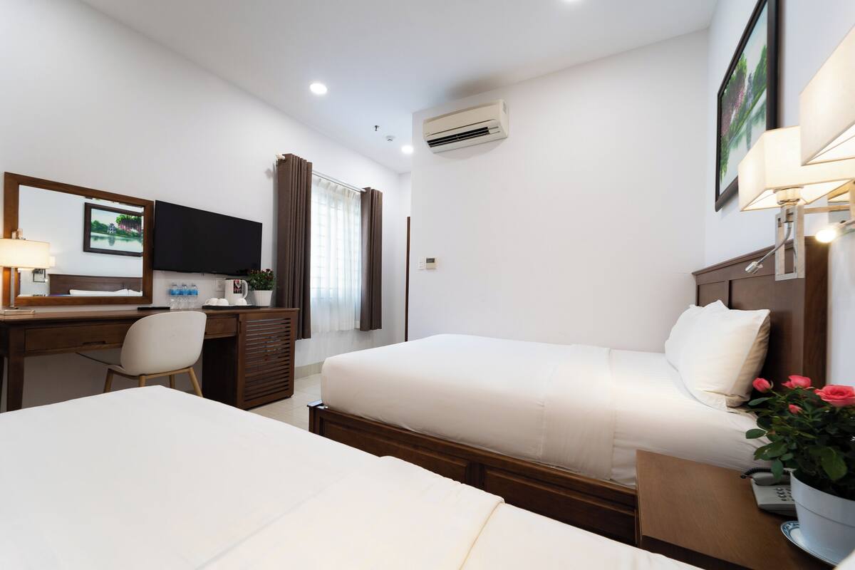 A hotel room with two beds, a desk with a chair, a TV, and a window with curtains.