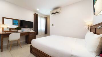 A hotel room with a bed, a desk with a chair, a flat-screen TV, an air conditioner, and a window with curtains.