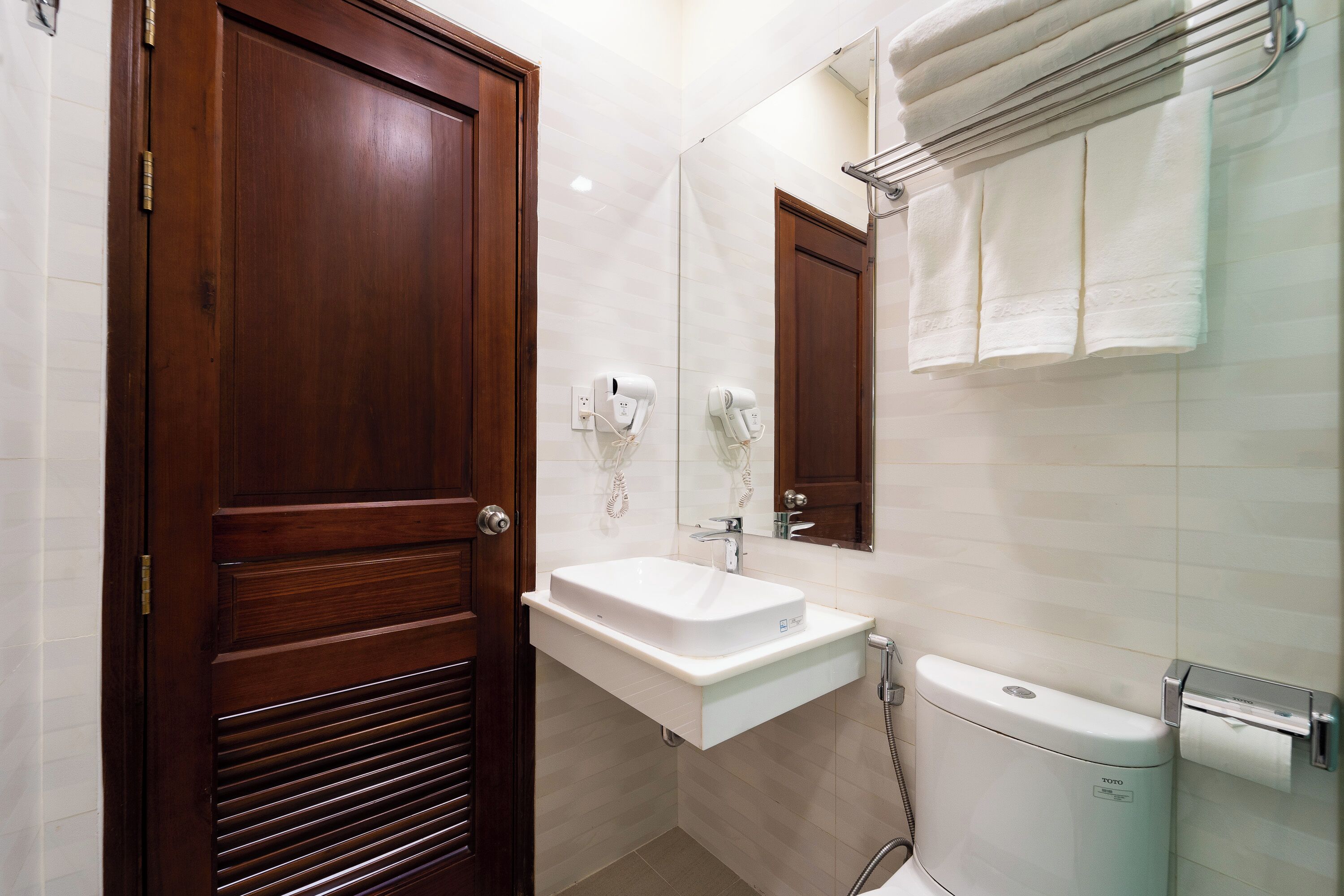 A bathroom with a wooden door, a white sink, a mirror, and a toilet.
