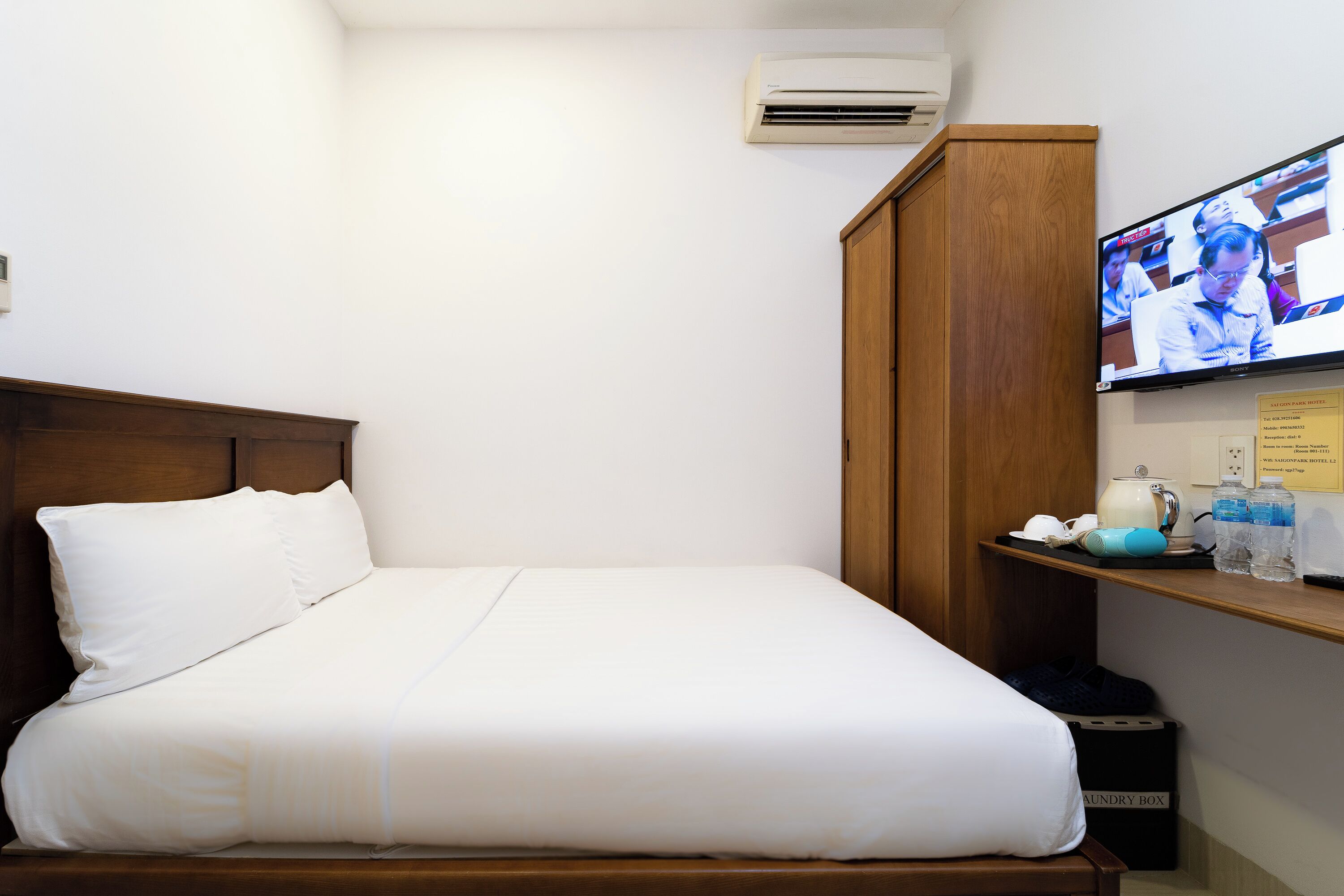 Ett hotellrum med en säng, en garderob i trä, en tv som är monterad på väggen och en hylla med toalettartiklar.