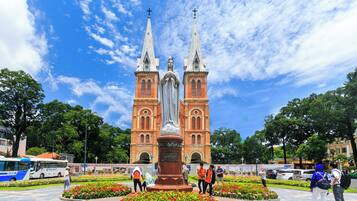 A historic church with two tall spires and a central statue, surrounded by a well-maintained garden with colorful flowers.