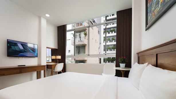 A hotel room with a large bed, a desk, a chair, a TV, and a window with a view of buildings. - Sai Gon Park Hotel (Ho Chi Minh City)