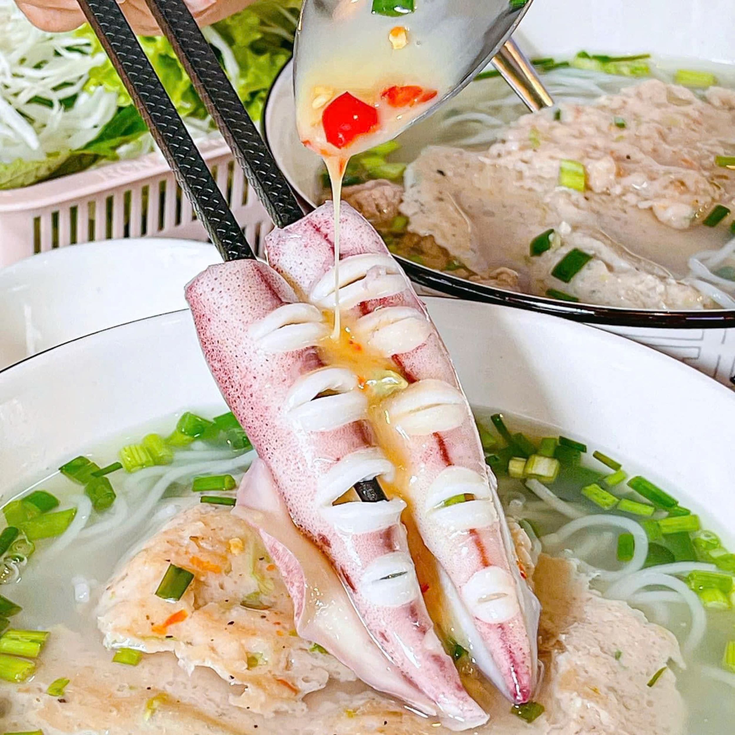 A bowl of noodle soup with a fish head and chopsticks.