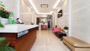 A hotel reception area with a wooden reception desk, a bench, a small table with a plant, and a wall-mounted TV. - Sai Gon Park Hotel (Ho Chi Minh City)