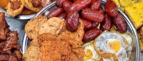 A variety of food items including grilled meat, sausages, fried eggs, and other dishes on a metal platter.