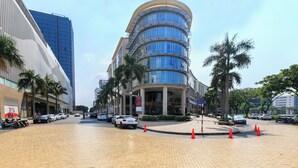 A modern building with a curved facade, palm trees, and a paved area with parked cars and orange traffic cones. - Sai Gon Park Hotel (Ho Chi Minh City)
