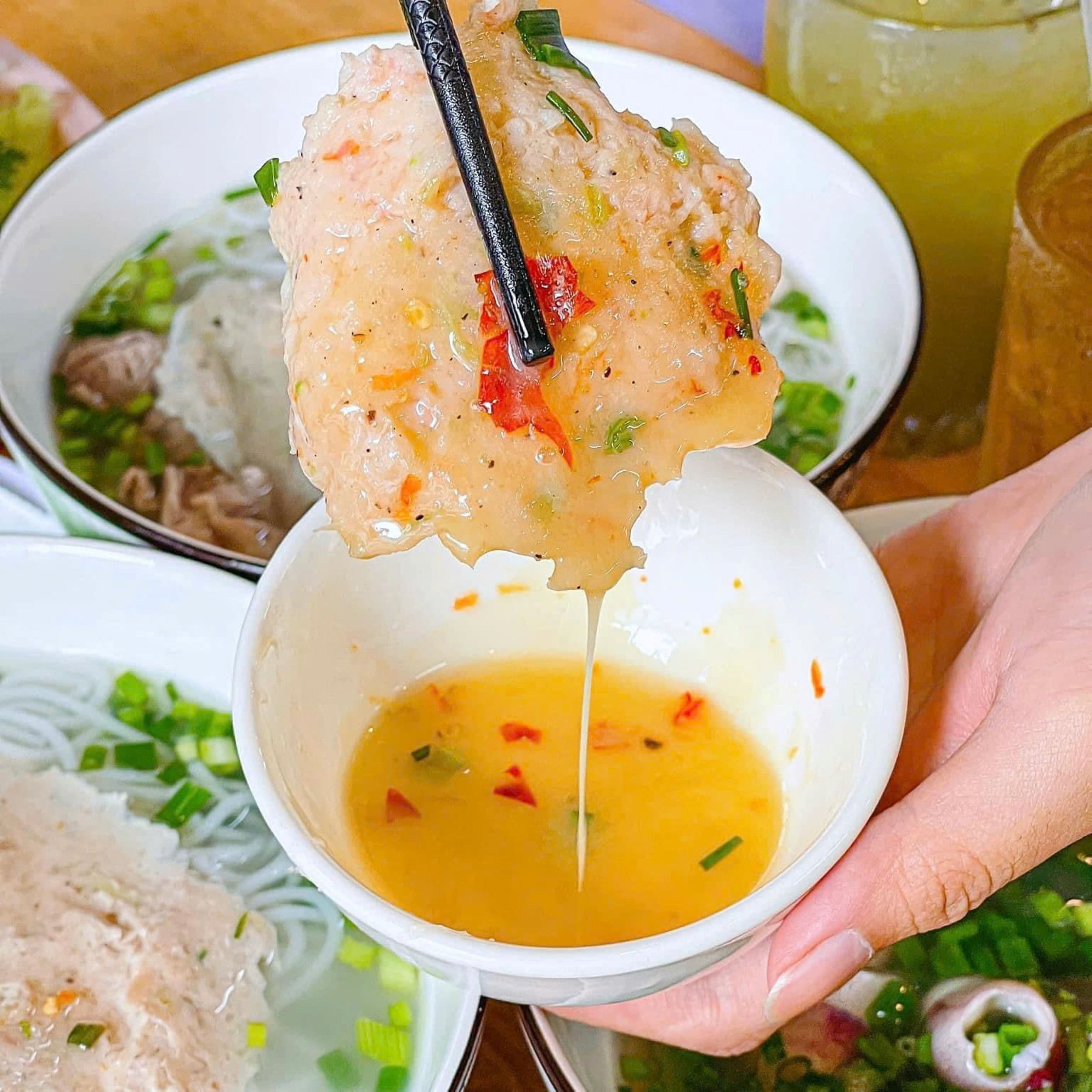 A bowl of soup with a dumpling being lifted with chopsticks.