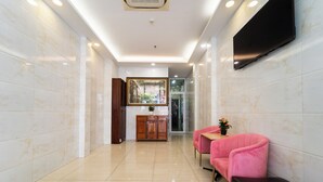 A hallway with a wooden cabinet, a pink sofa, and a TV mounted on the wall. - Sai Gon Park Hotel (Ho Chi Minh City)