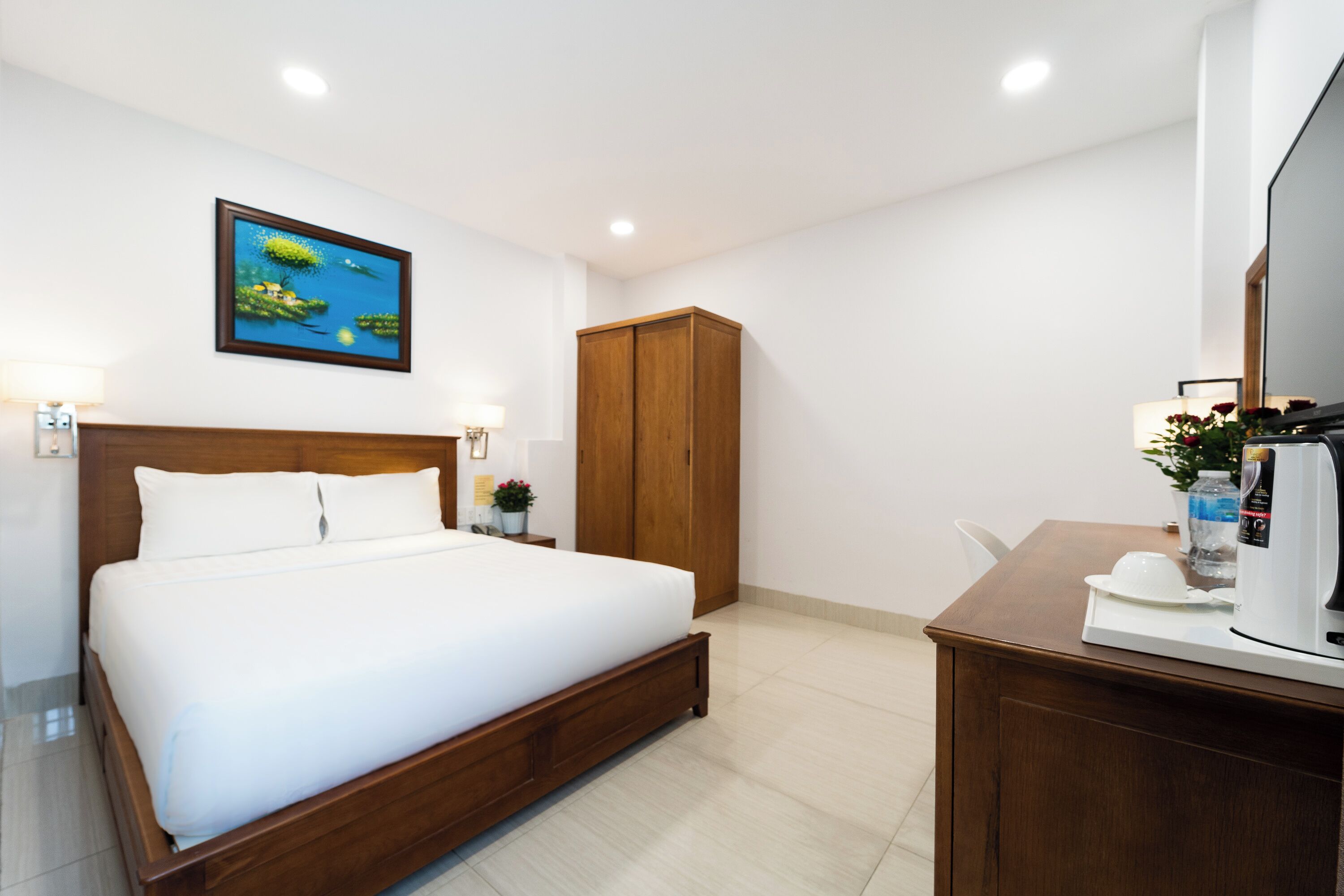 A hotel room with a wooden bed, a wardrobe, a desk with a coffee maker, and a framed picture on the wall.