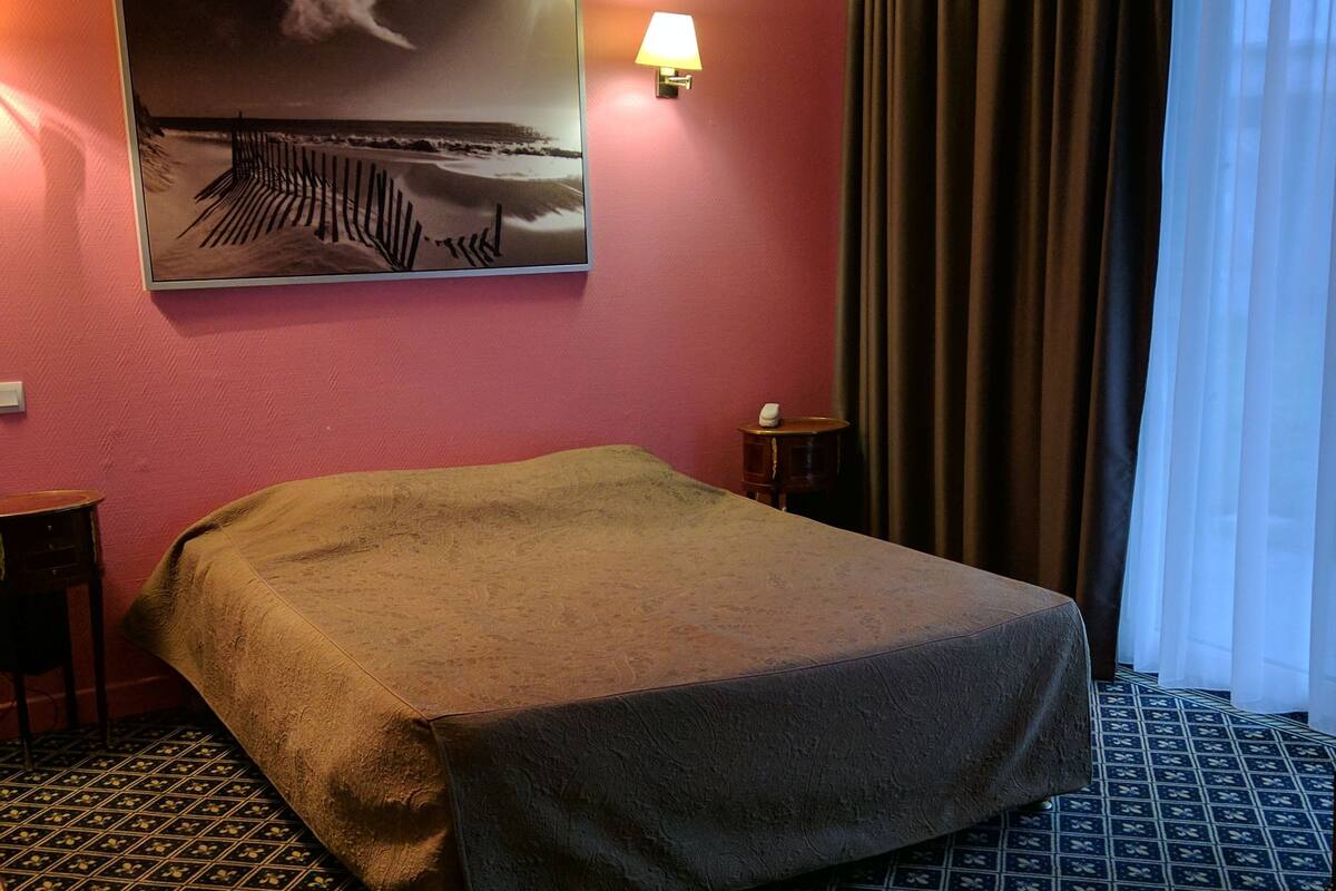 Een hotelkamer met een bed, een aan de muur hangend schilderij, een lamp, een klein tafeltje en een vloer met een patroon.
