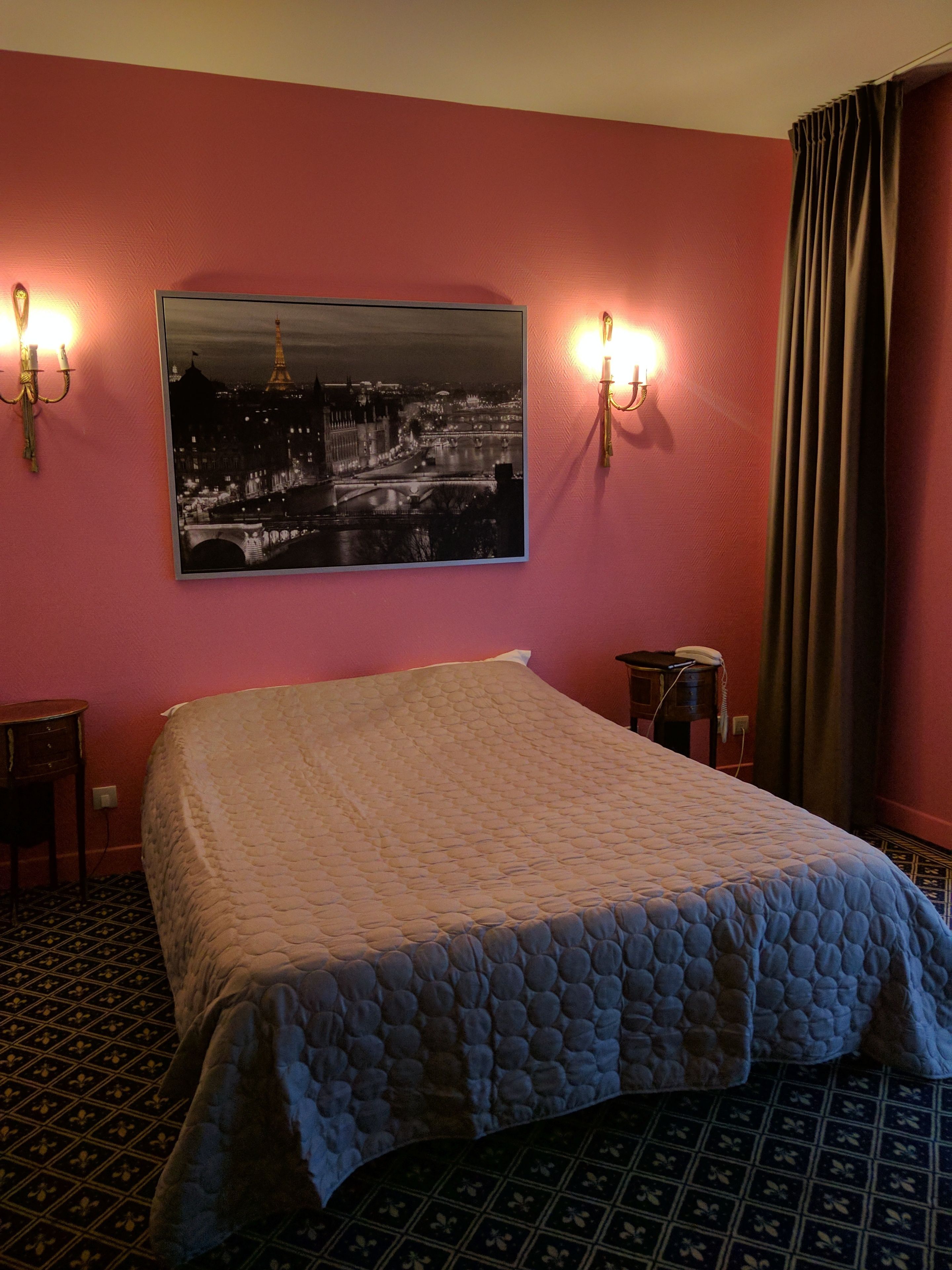A hotel room with a bed, a nightstand, a telephone, and a wall-mounted picture of a cityscape.