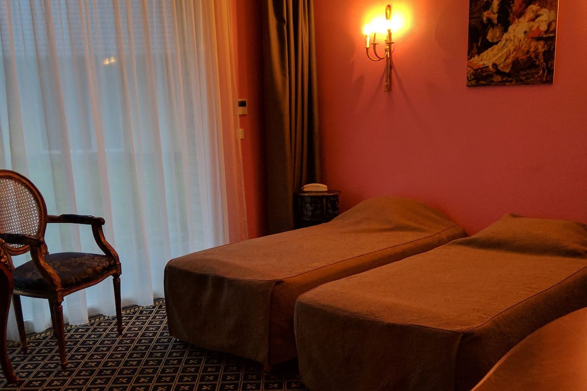 Een hotelkamer met twee enkele bedden, een houten stoel, een tafeltje, een wandlamp en een schilderij.