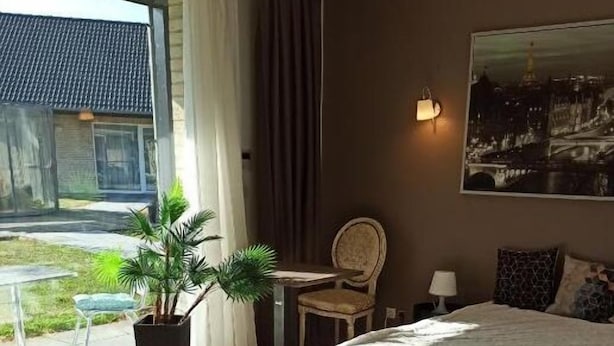 Een hotelkamer met een groot bed, een bureau, een stoel, een kamerplant en een stadsgezichtschilderij aan de muur.