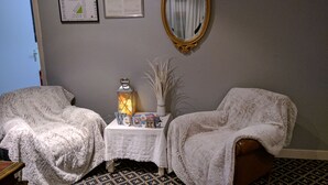 Een kamer met twee fauteuils, een tafeltje met een lantaarn, en een spiegel aan de muur.