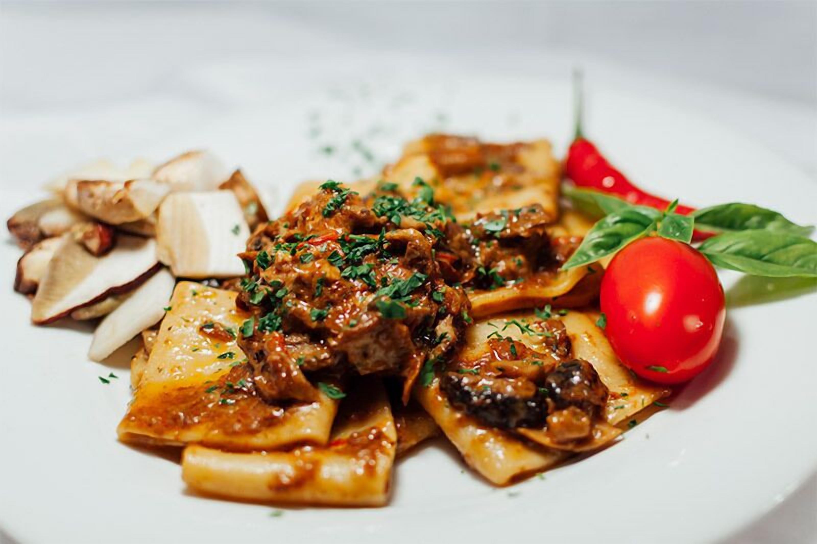 A plate of pasta with mushrooms and a cherry tomato garnish.