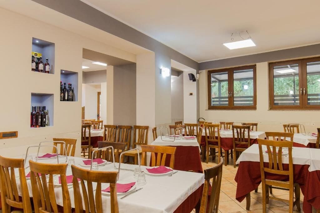 A dining area with multiple tables and chairs, some with red tablecloths. There are shelves with bottles on the walls.