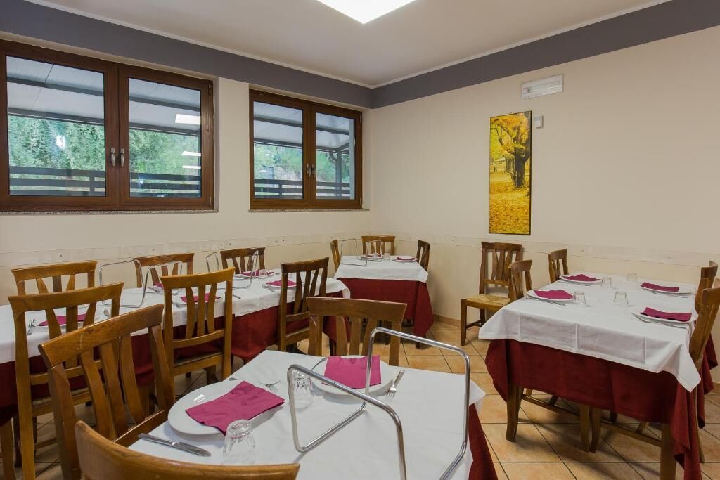 Comedor con mesas dispuestas para cuatro personas, sillas de madera y ventanas amplias con vistas a la vegetación.