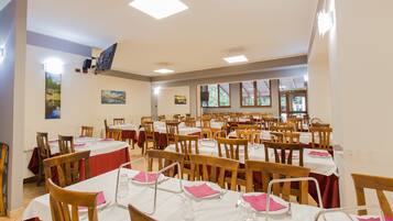 Un espace repas avec plusieurs tables et chaises, des nappes blanches et des serviettes rouges.