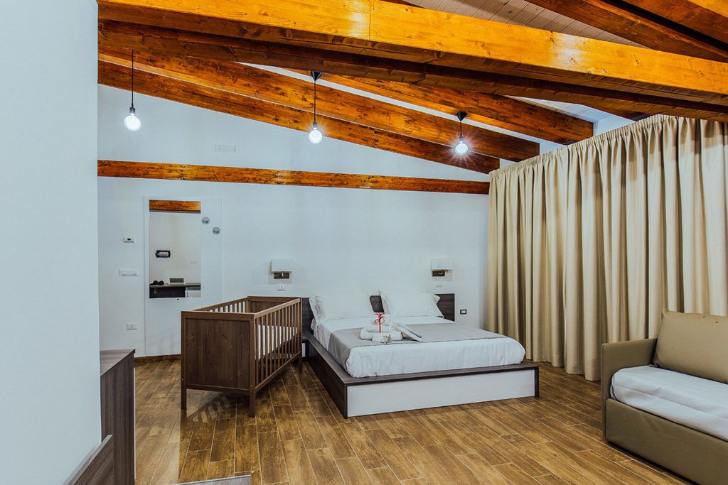 Un dormitorio con techo de madera, una cama, una cuna, un sofá y una cortina.