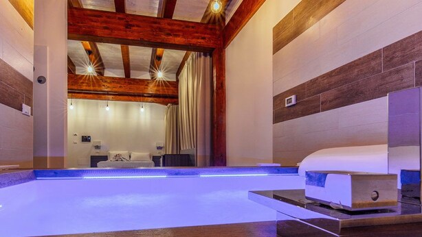 Une salle de spa moderne avec un plafond en bois, une piscine illuminée de lumière bleue et une table de massage.